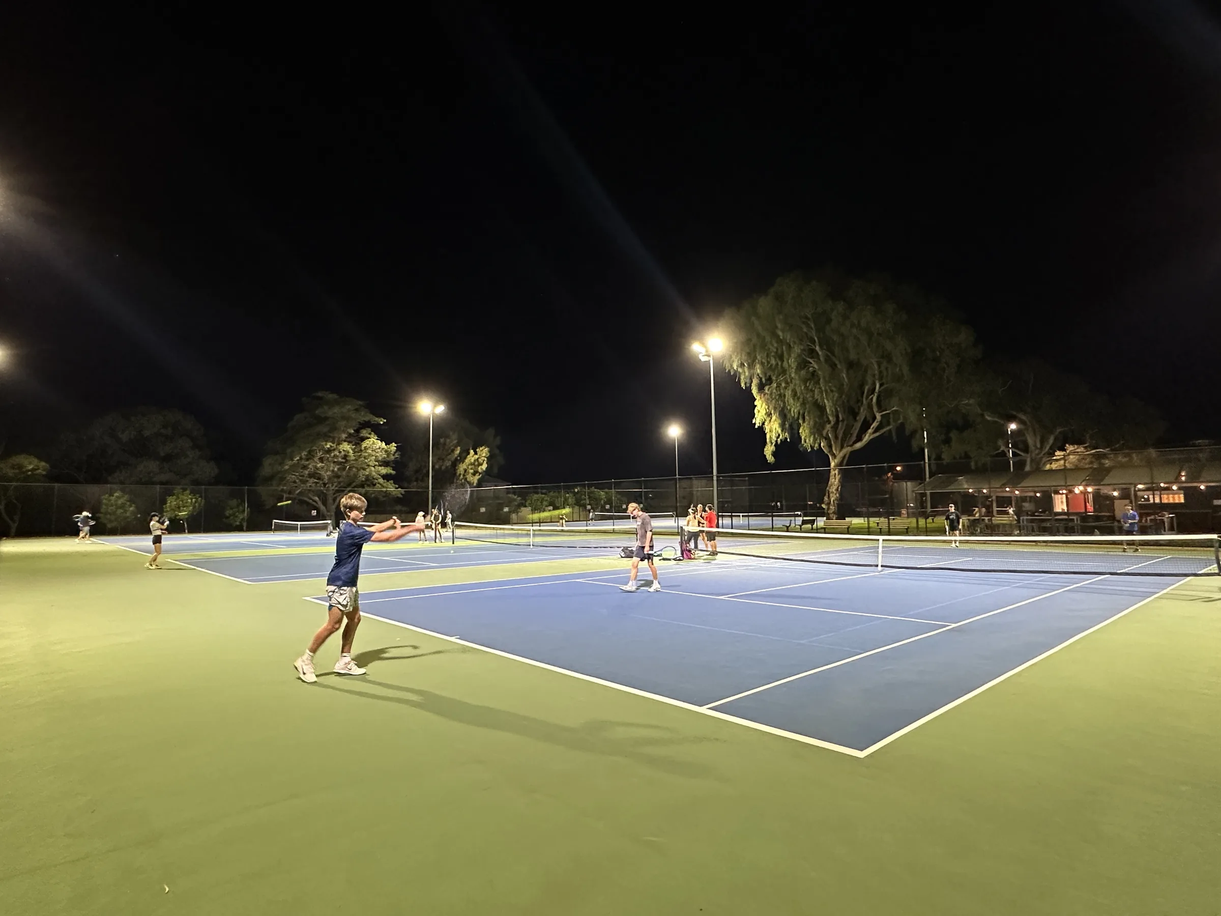 Junior player hitting a forehand during a night session at the club