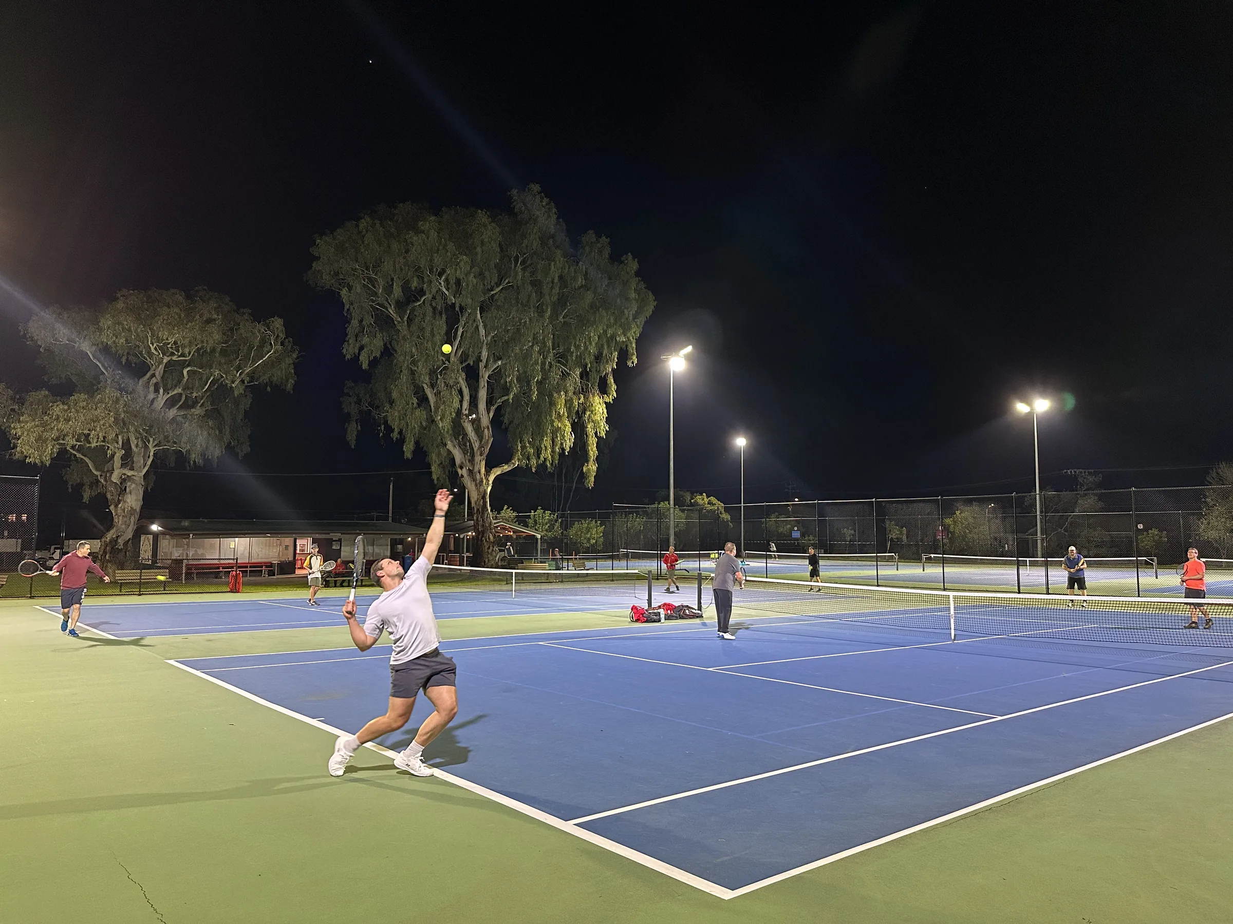 Players serving and rallying under lights at the club